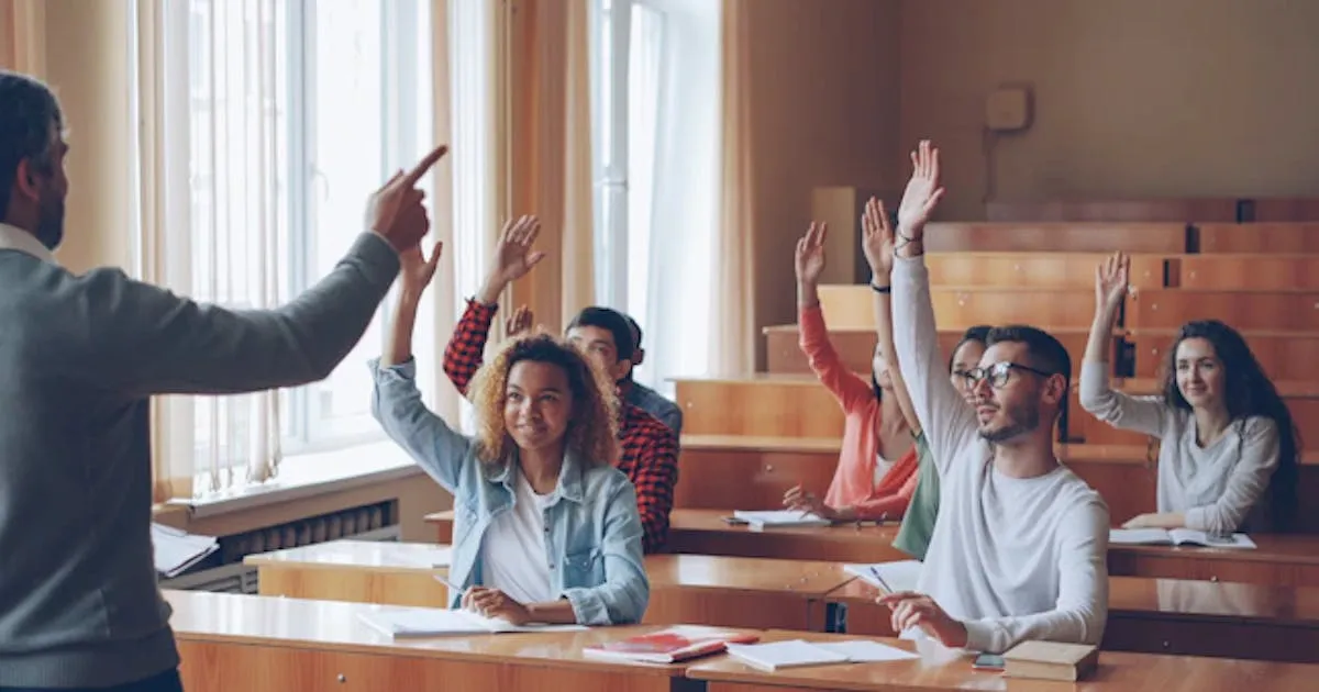 Teacher pointing at students with raised hands in lecture hall.
