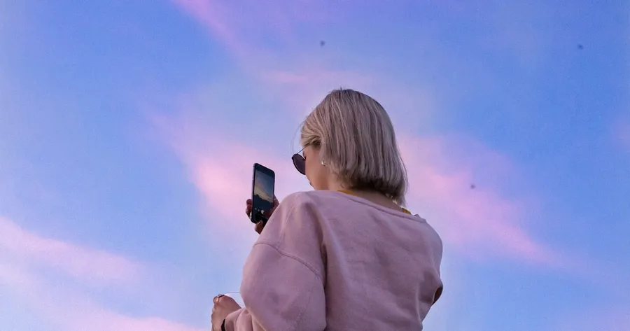 woman in sunglasses and pink top holding phone