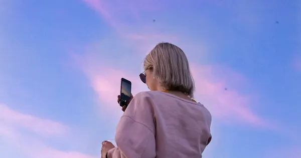woman in sunglasses and pink top holding phone