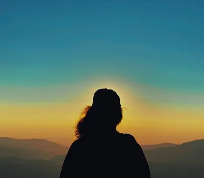 silhouette of woman standing on top of mountain during sunset