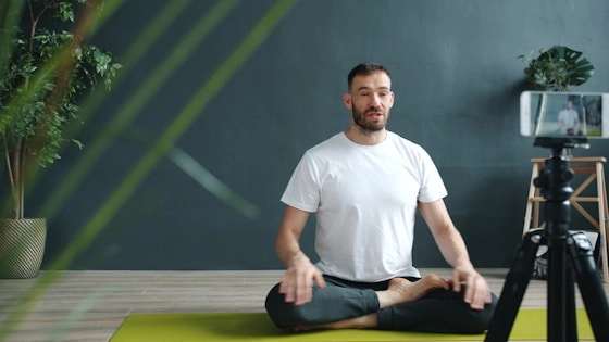 Man meditating on yoga mat recording with phone.