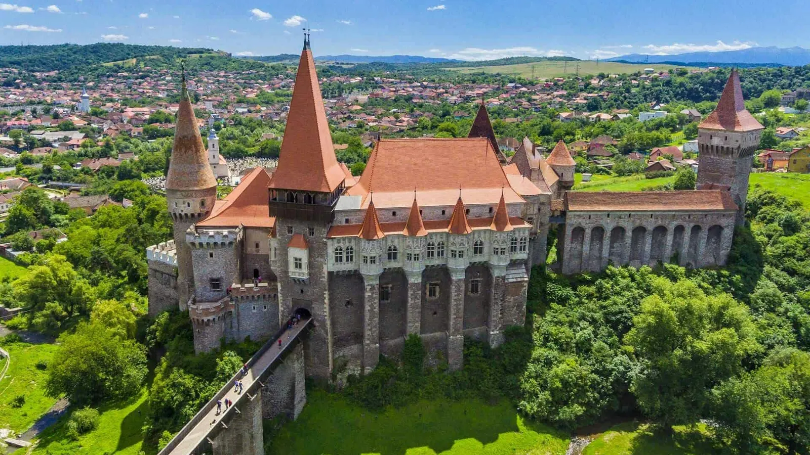grey castle surrounded by green trees and a blue sky